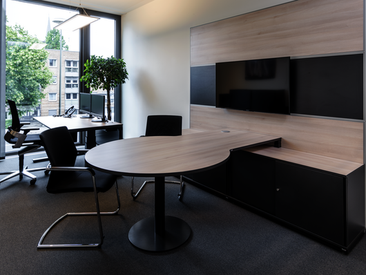 Sitz-Steh-Tisch WINEA PRO Beraterplatz und WINEA MAXX Scheibentürenschrank mit einem Besprechungstisch