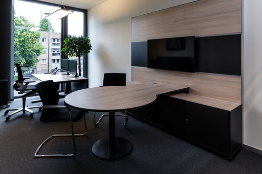 Sitz-Steh-Tisch WINEA PRO Beraterplatz und WINEA MAXX Scheibentürenschrank mit einem Besprechungstisch