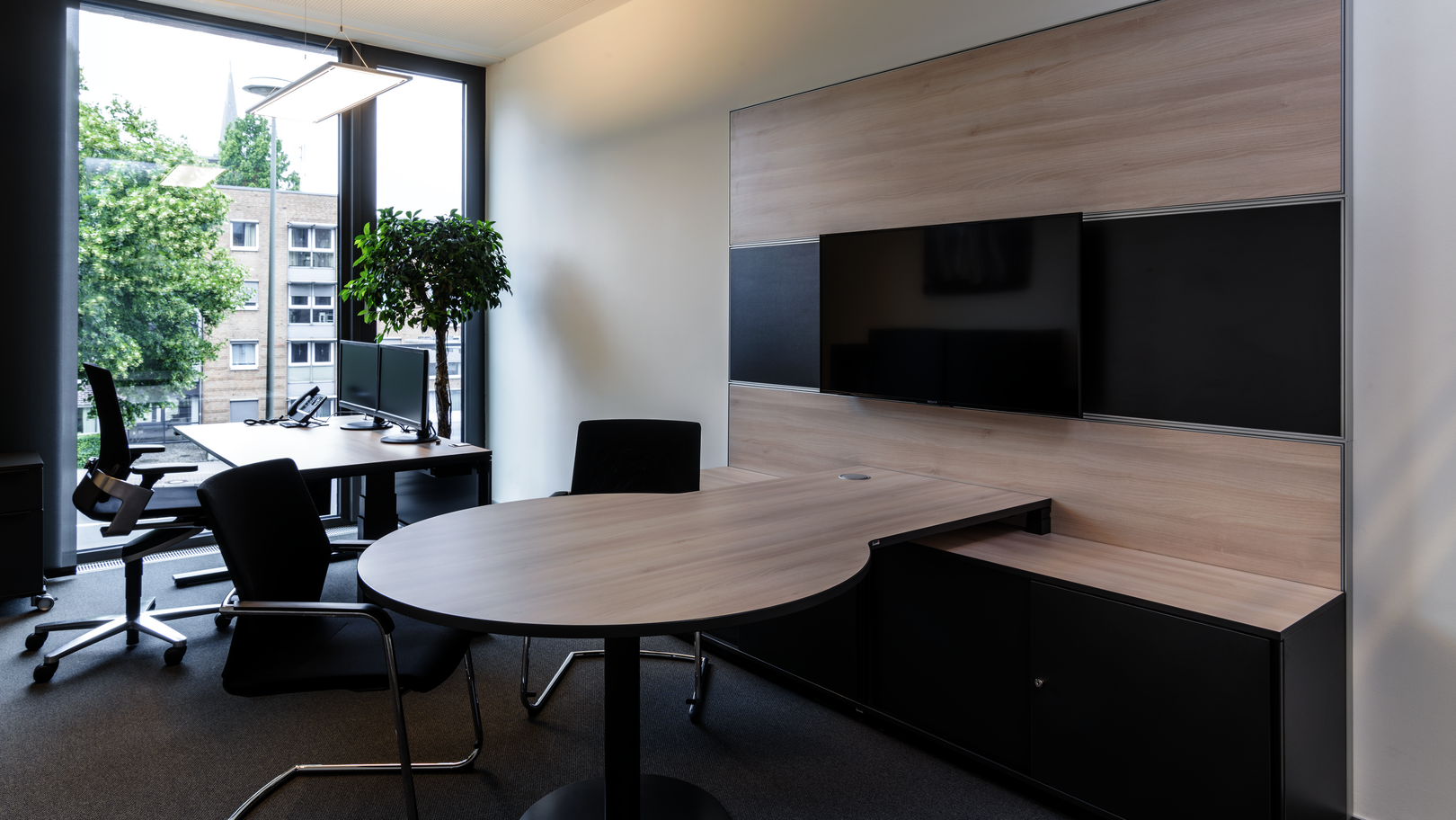 Sitz-Steh-Tisch WINEA PRO Beraterplatz und WINEA MAXX Scheibentürenschrank mit einem Besprechungstisch