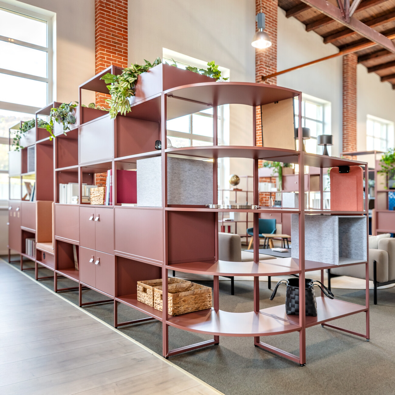 Diese Mittelzonen-Lounge ist geprägt von den rostroten, raumgestaltenden WINEA MAXX Regalen mit Flügeltüren, neuen Griffen, Pflanzaufsätzen sowie dem  integrierten Mülltrennsystem. WINI Forum Sandsteinhalle, Ausstellung zur Hausmesse 2025