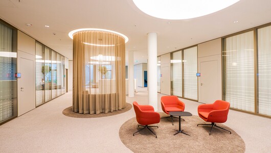 Besprechungstisch in Sitzhöhe auf Teppich mit roten Sitzmöbeln