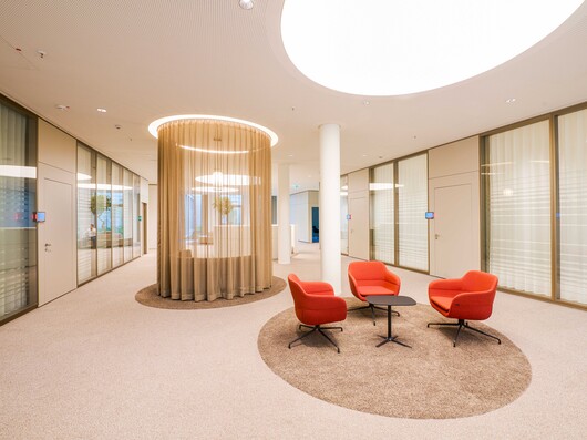 Besprechungstisch in Sitzhöhe auf Teppich mit roten Sitzmöbeln