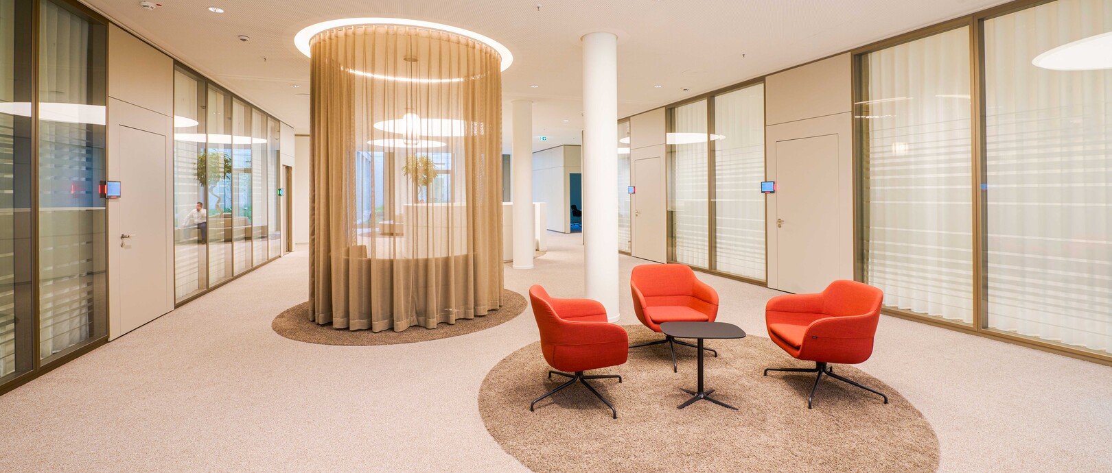 Besprechungstisch in Sitzhöhe auf Teppich mit roten Sitzmöbeln